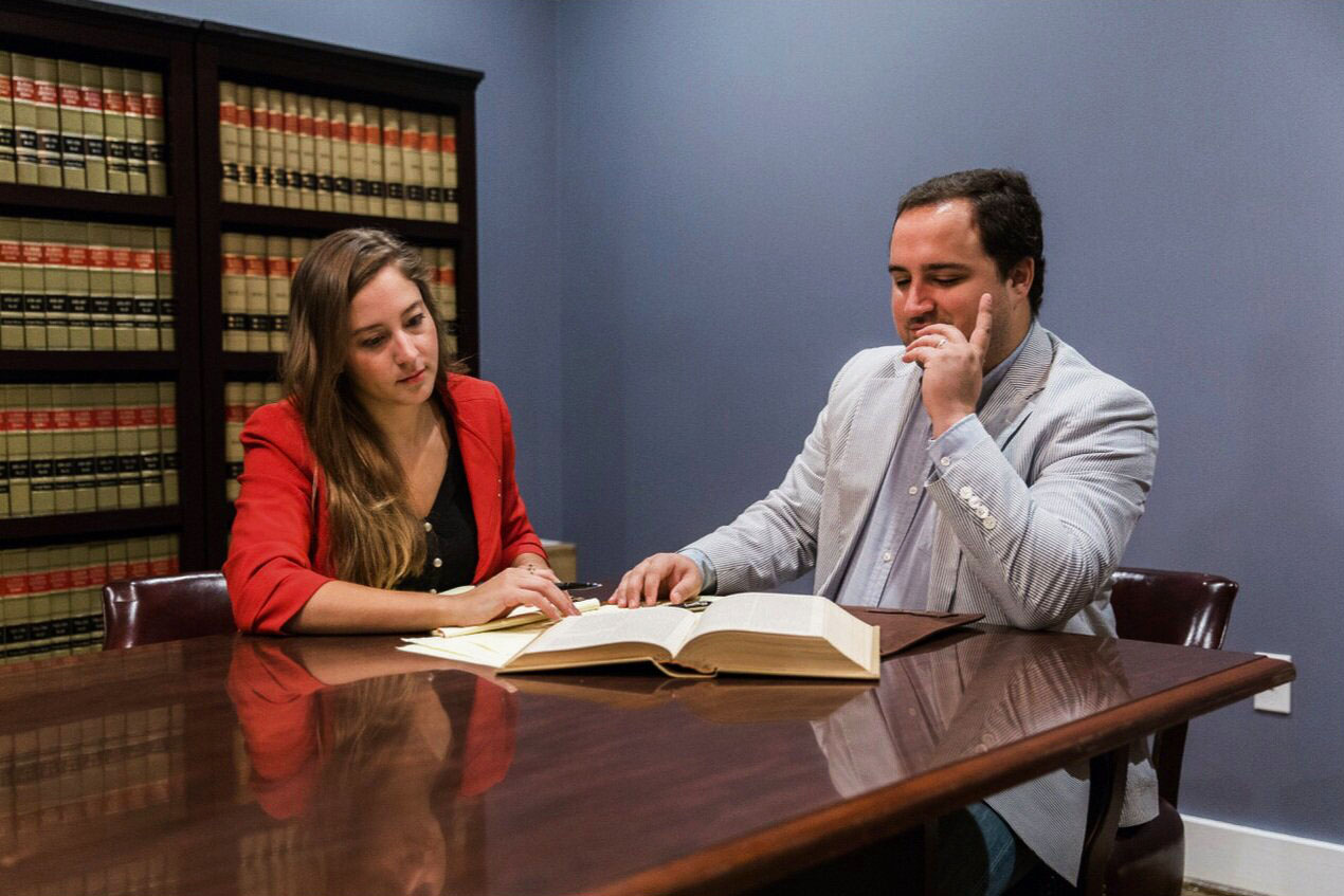 Alyssa Enzor Baxley and Adam Maniscalco, two attorneys at law practicing with Baxley Maniscalco, LLP, sit at a wooden desk in a conference room, examining case details.