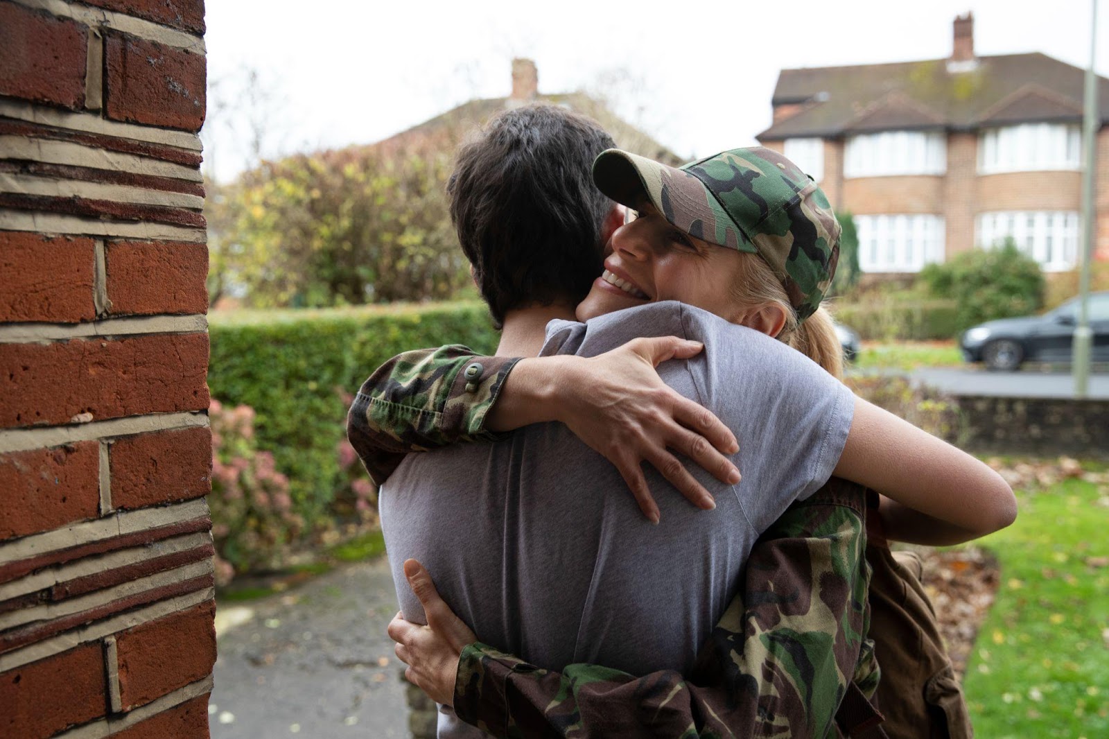 A military woman in camouflage hugging a loved one outside their home, smiling warmly. The embrace captures the emotional connection and support military families share, symbolizing how Alabama law helps ensure access to online learning resources for military families.