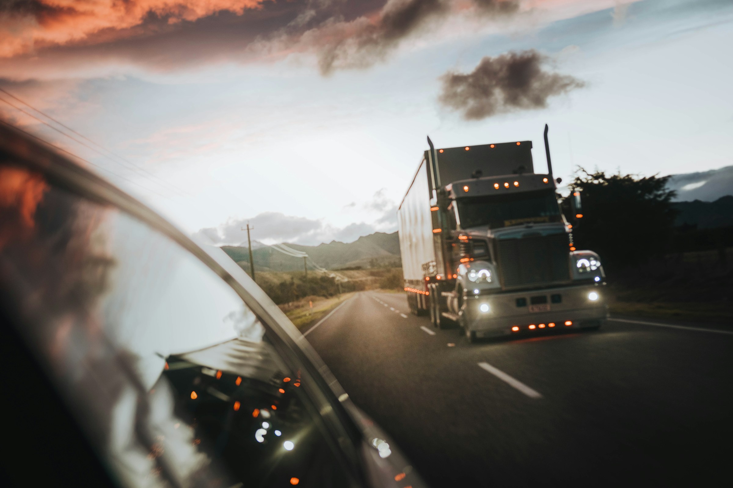 Two trucks are seen driving down the highway during sunset.