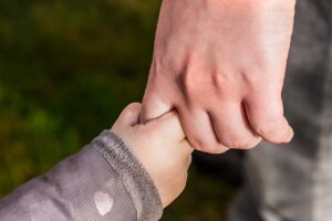 A parent, seeking child custody, holds the hand of their child as they face an uncertain future.