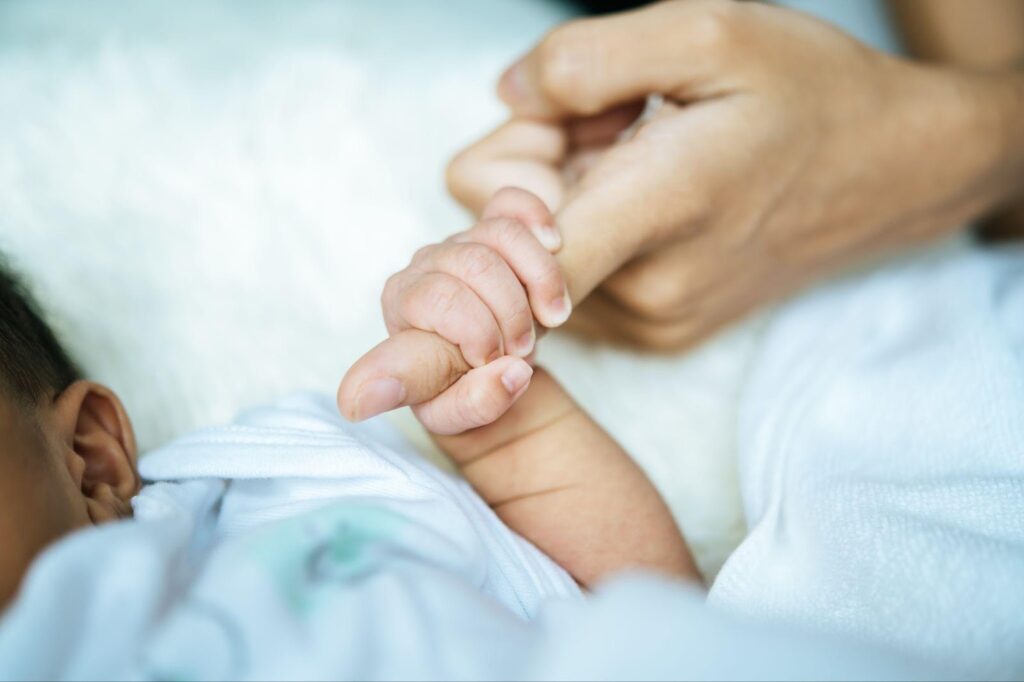 Newborn baby's tiny hand grasping mother's index finger, symbolizing trust and the precious bond between parent and child.