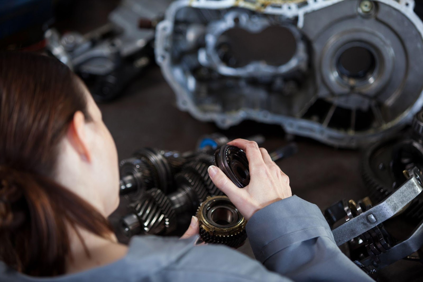 Woman inspecting car engine, holding diagnostic tool, with open hood in the foreground.