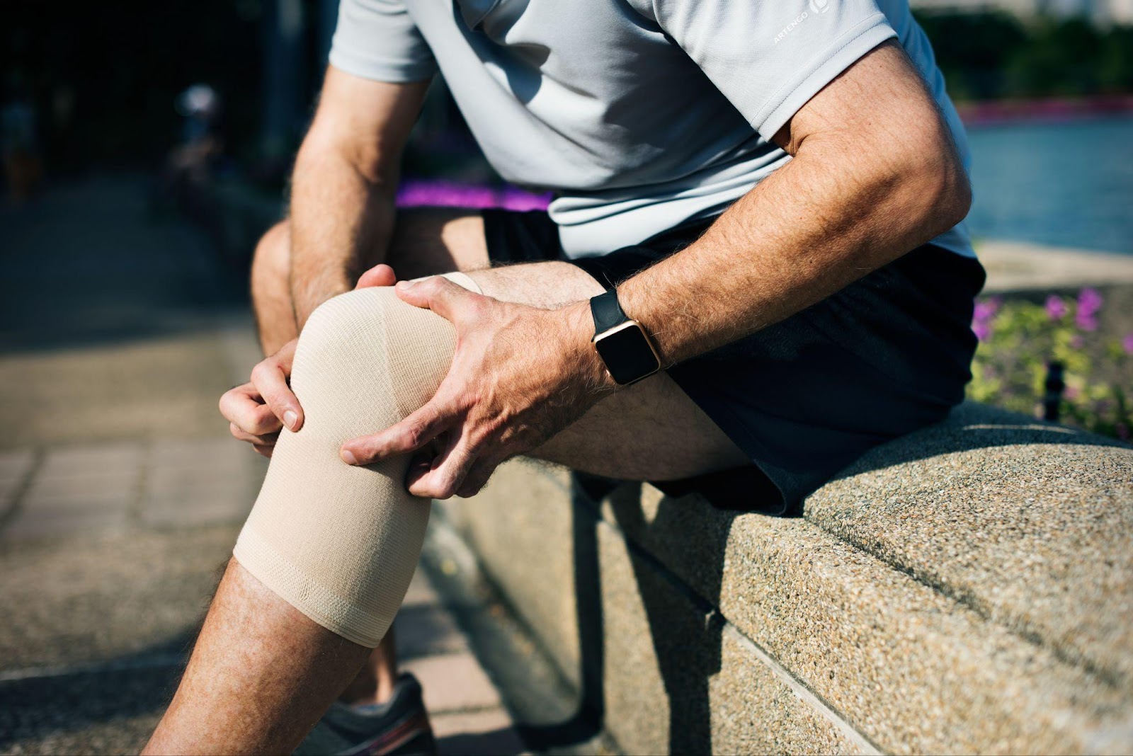 Person grimacing while holding their knee, suggesting pain from a possible injury or pre-existing condition.