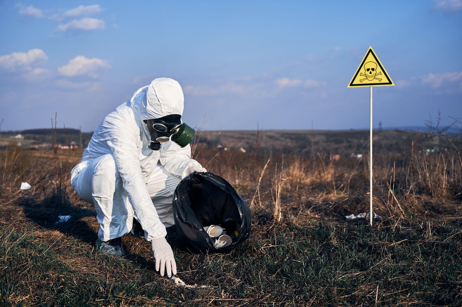 Environmentally conscious volunteer in protective gloves collecting litter from a grassy area, demonstrating community cleanup efforts.