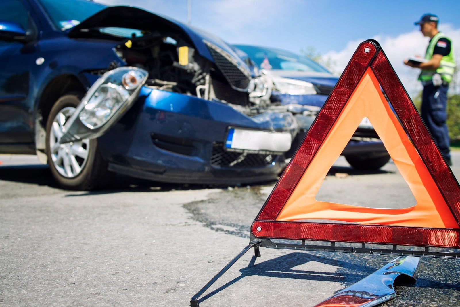 Policeman writing report at intersection accident scene, caution triangle sign in foreground.