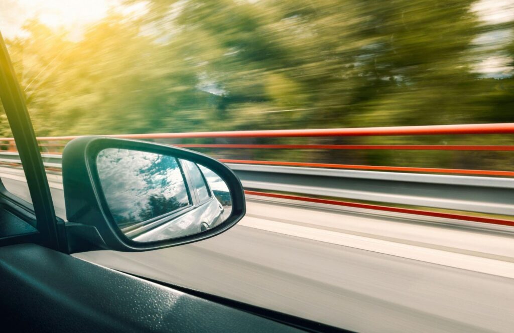 Alert driver with hands on steering wheel, focused on road ahead through windshield of moving car.