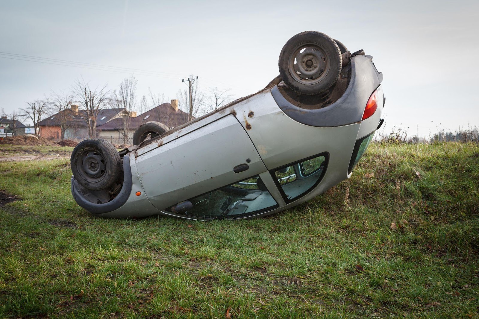 Overturned hatchback on its roof by roadside, aftermath of severe rollover accident.