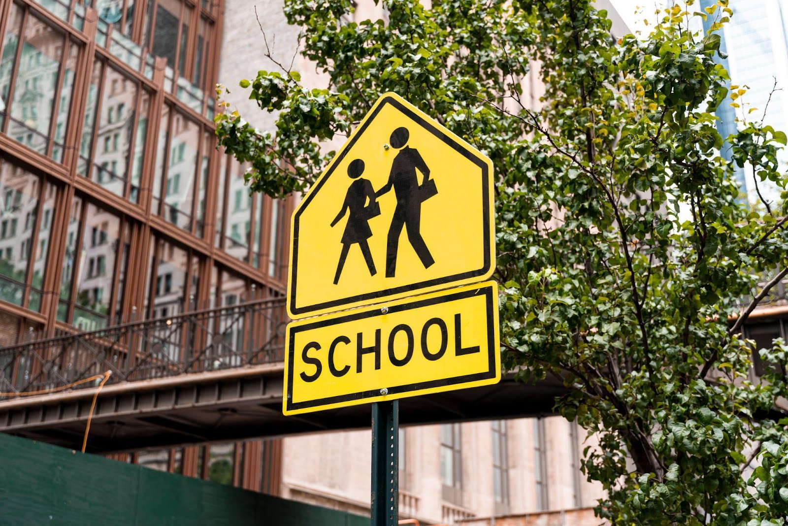 Yellow diamond-shaped road sign with black silhouettes of children walking, accompanied by the words “SCHOOL” in bold black letters.