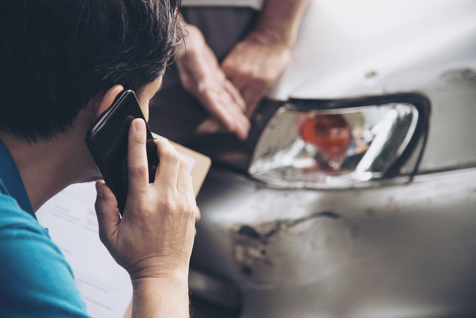 Distressed person on phone looking at damaged vehicle after car accident.