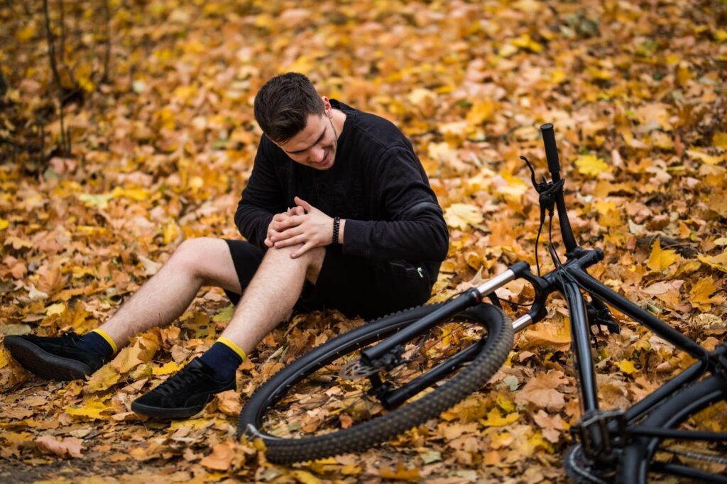 A person sitting on the ground, holding their knee in pain, next to a bicycle, likely after an accident.