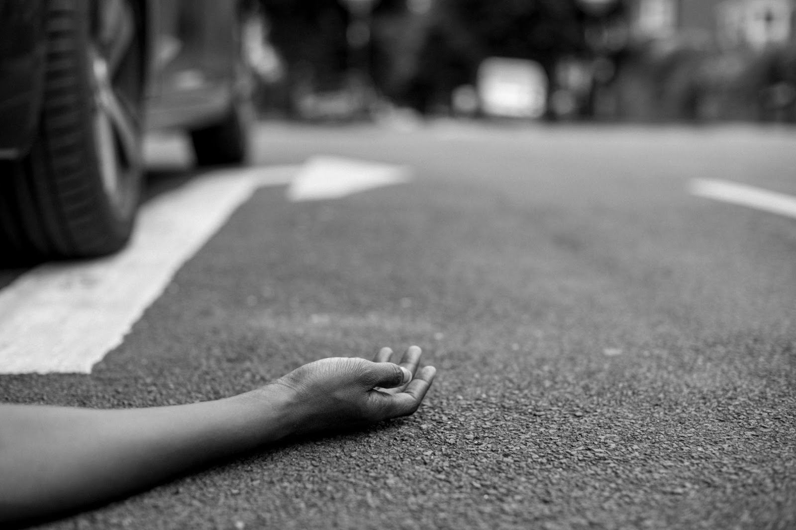 Injured pedestrian lying on road after accident, surrounded by concerned onlookers.