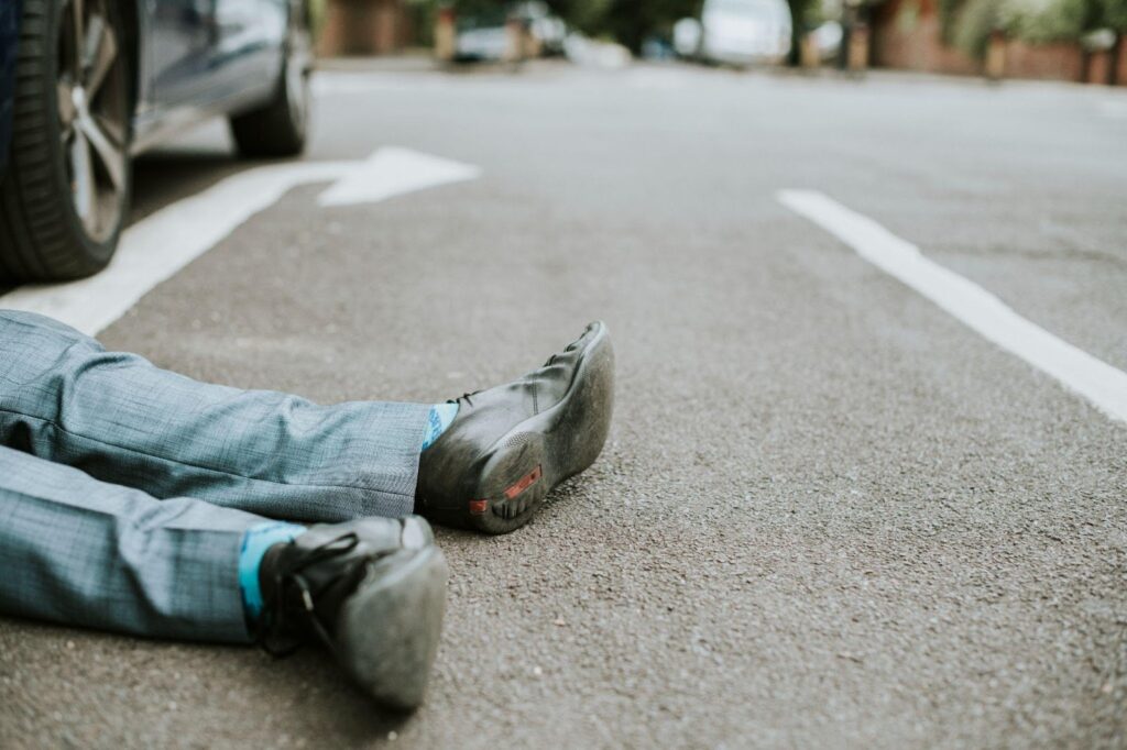 Injured pedestrian lying on crosswalk after accident, surrounded by concerned bystanders.