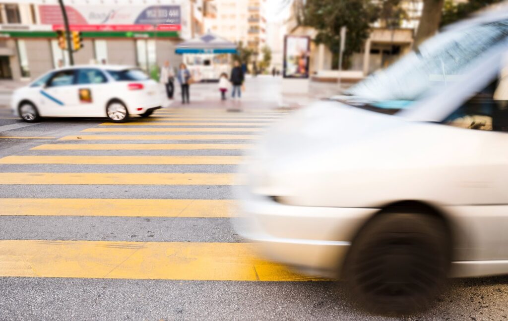 Car speeding away from fallen pedestrian on crosswalk, leaving trail of smoke.