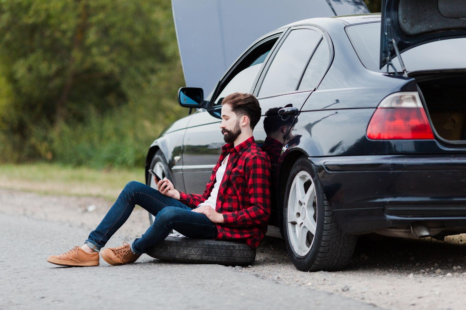 A frustrated driver sits on his phone beside his damaged car after a rear-end collision on an Alabama highway.