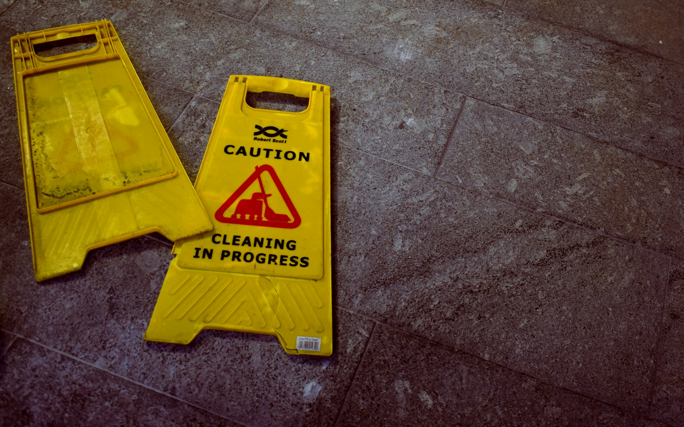 A "Caution: Cleaning in Progress" sign lies on the floor outside a business premises.