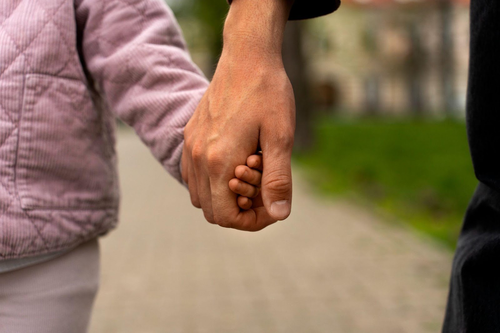 A close-up view of a child's small hand gently clasped in the larger hand of an adult, symbolizing trust, guidance, and the parent-child bond.