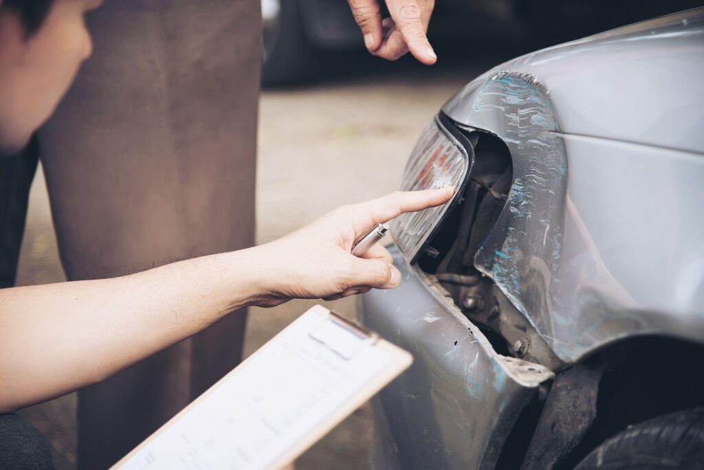 Insurance adjuster in a suit taking notes on a clipboard while examining a damaged vehicle at a T-bone accident scene.