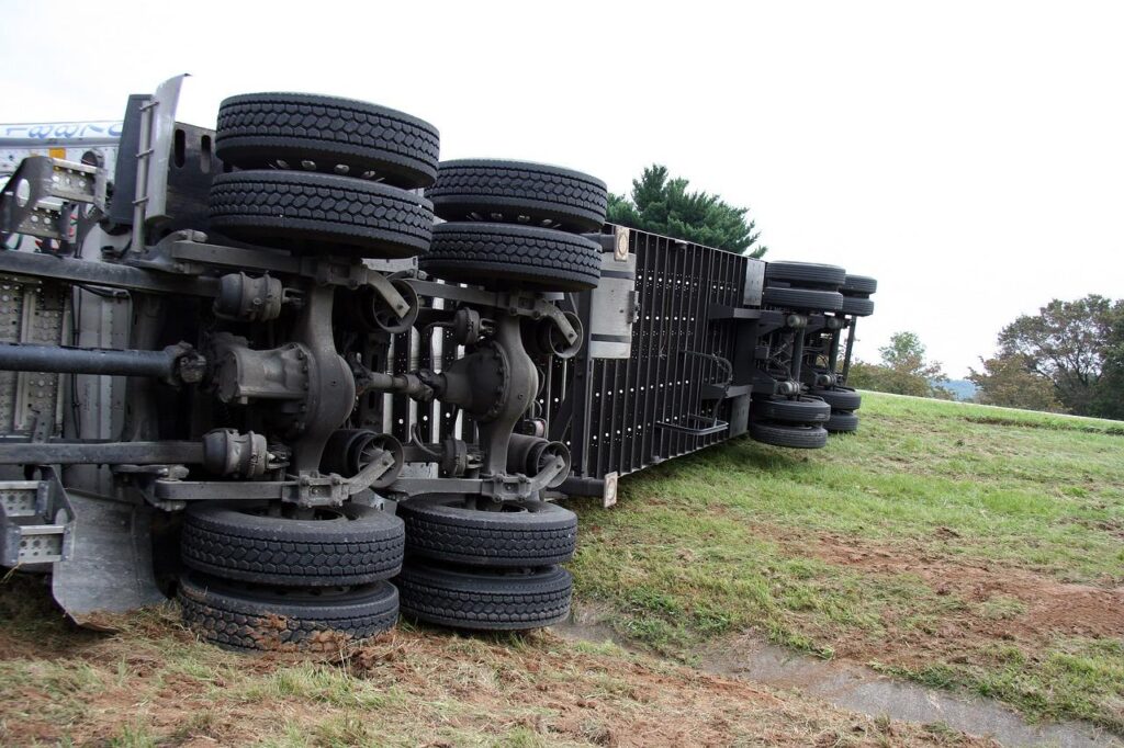 Side view of a truck that has been involved in a severe accident, lying on its side with visible damage from the crash.