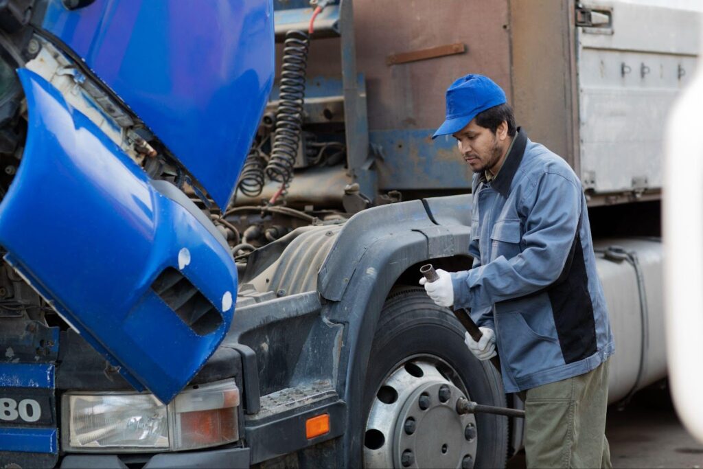 A mechanic examines the tire and engine area of a large truck, possibly checking for damages or maintenance after a truck accident.