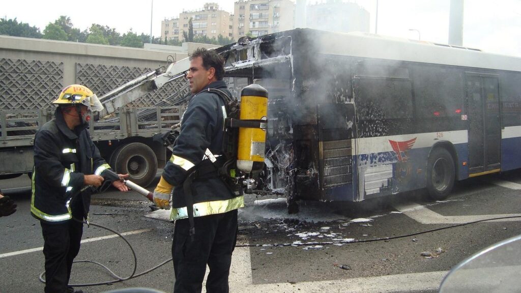 Bus accident scene with two firefighters extinguishing flames, illustrating emergency response efforts after a severe collision.