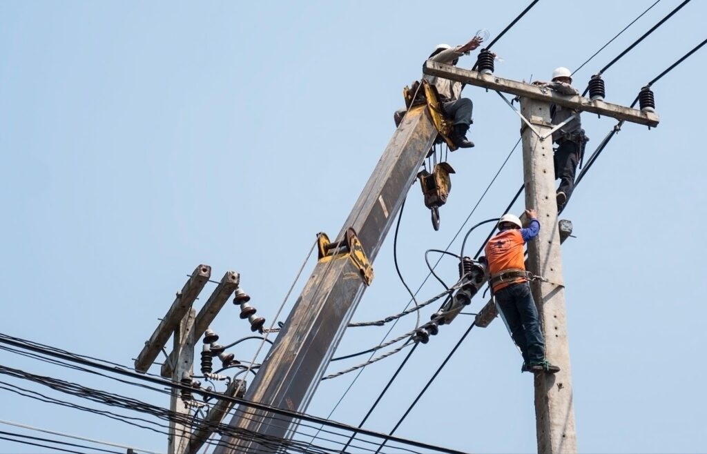 Construction workers are performing tasks on elevated electrical poles, highlighting the risks of electrocution and the importance of adhering to electrical safety regulations.