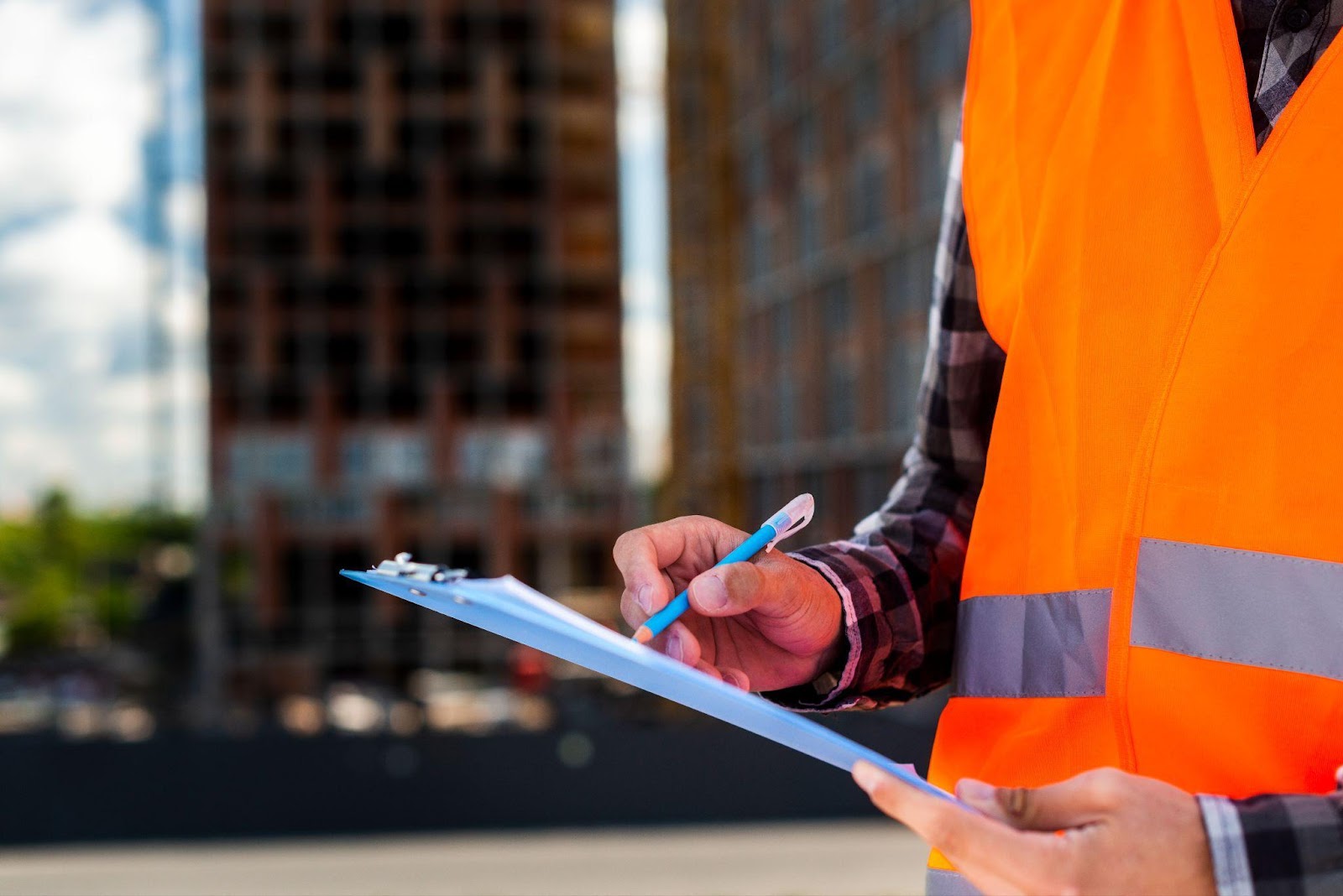 A close-up of a person holding a clipboard and pen, taking notes on OSHA regulations at a construction site.