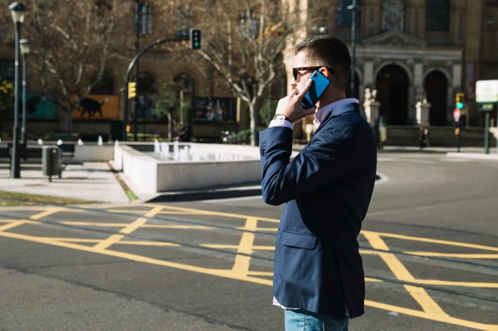 A person walks along a busy street while speaking on the phone, representing a distracted pedestrian. The individual's attention is focused on the phone, illustrating the risks of not paying attention to the surroundings while walking.