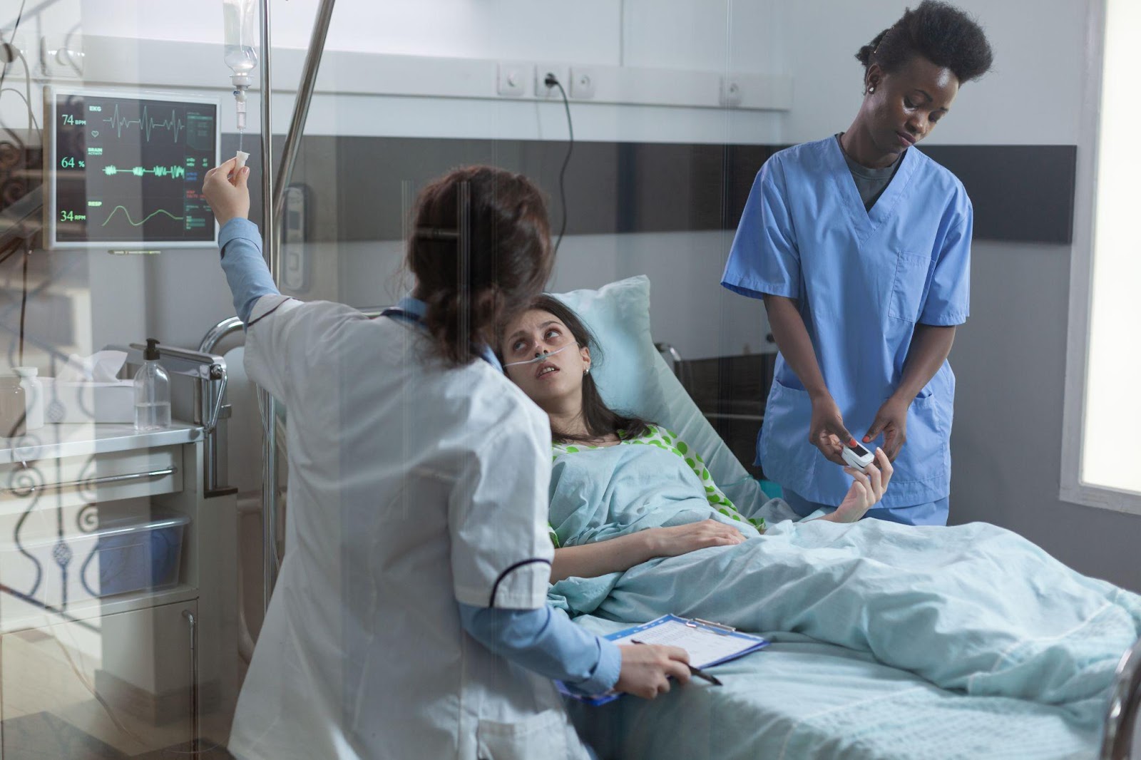 Two medical professionals attending to a patient in a hospital bed: one nurse placing a pulse oximeter on the patient's finger, while a doctor adjusts an IV drip.