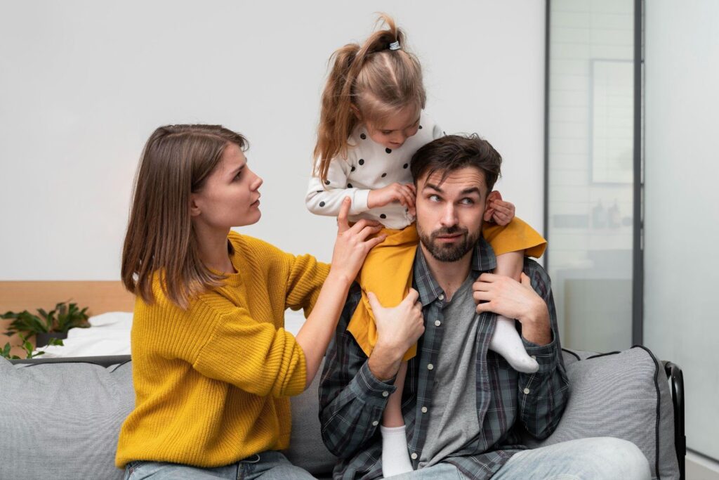 A playful family moment featuring a father with his daughter sitting on his shoulders as the mother adjusts her.