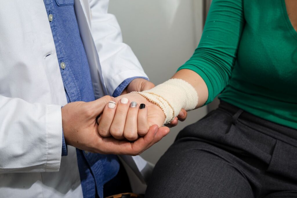 A close-up image of a medical professional gently holding the bandaged hand of a patient during a check-up.