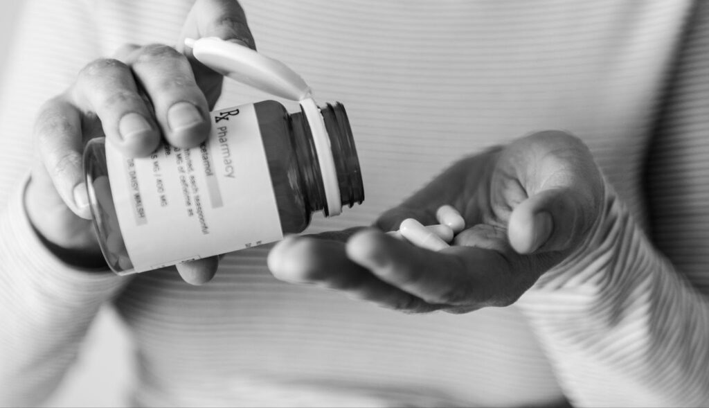 Close-up of a woman's hand pouring pills from a bottle into her palm, emphasizing the importance of awareness around drug interactions and safe medication practices.