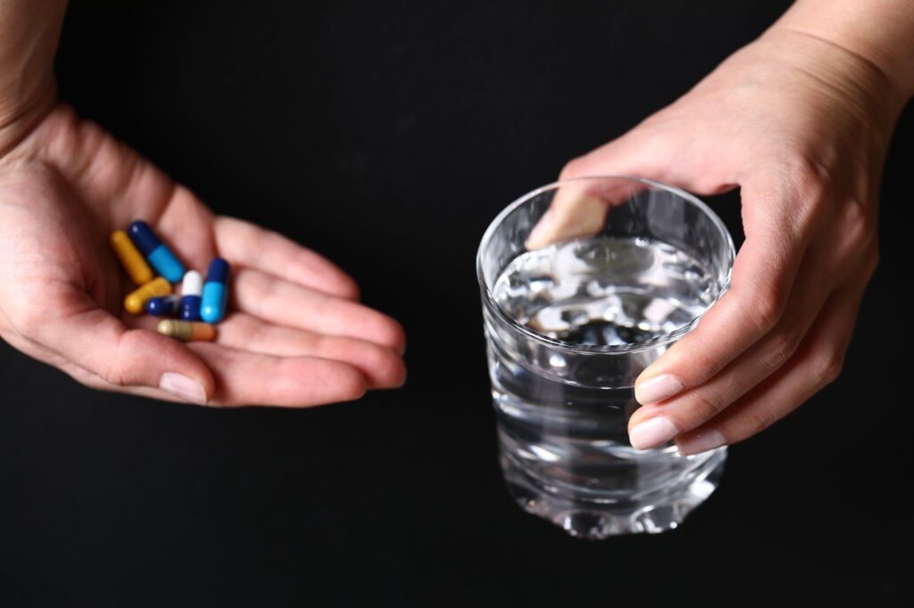 A hand holds a few pills above a cup of water, symbolizing the act of taking medication. The image highlights the potential risks associated with dangerous drugs, emphasizing the importance of awareness and caution when using pharmaceuticals.