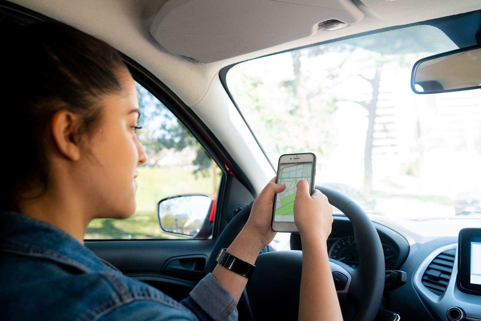 A person checking Google Maps on a smartphone while driving, highlighting the dangers of GPS and navigation system distractions in the context of distracted driving.