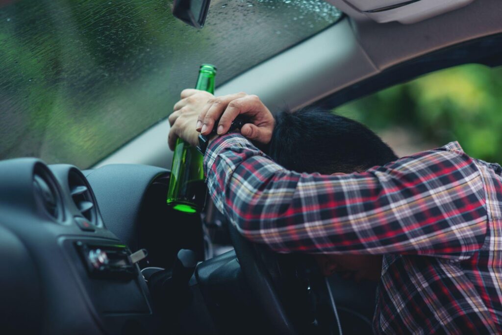 A person drinking from a bottle while driving, highlighting the dangers of drunk driving and the DUI laws and criminal charges enforced in Alabama.