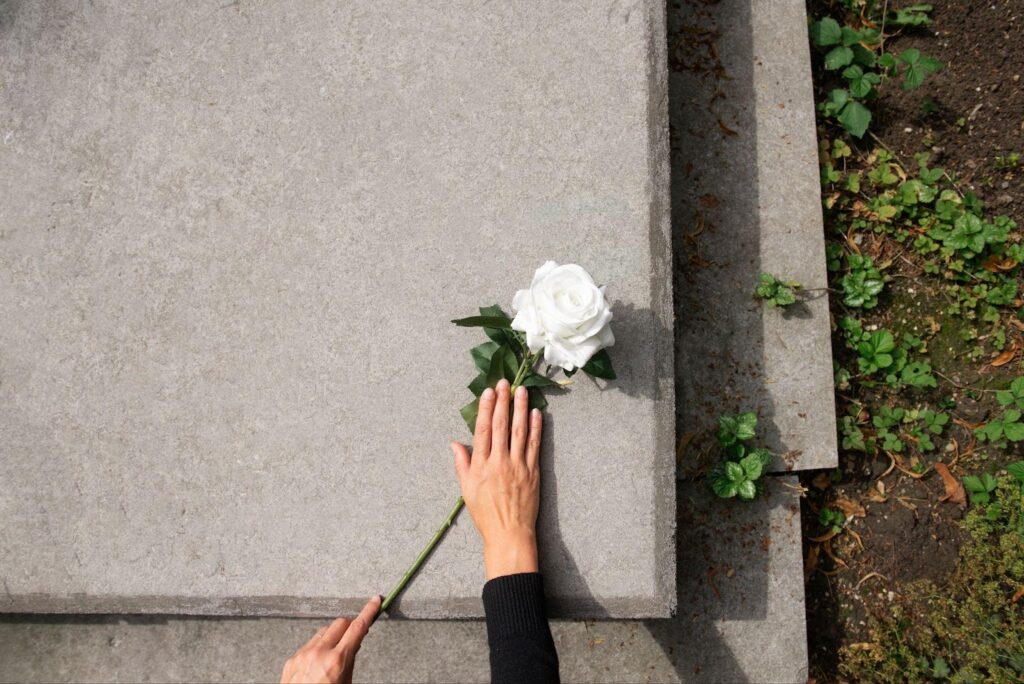 A hand gently places a flower on a tombstone, symbolizing remembrance and loss. The image conveys the sorrow associated with wrongful death claims, emphasizing the pursuit of justice for a loved one's untimely passing due to negligence.