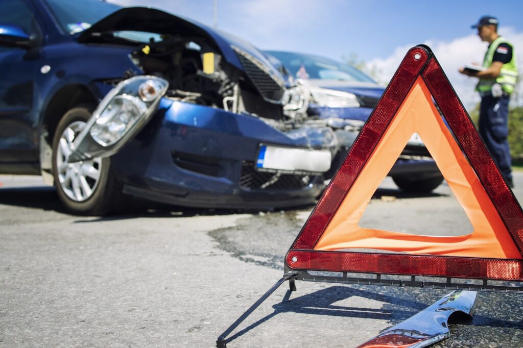 Scene of a car accident with visible damage to vehicles and a warning triangle in the foreground, representing the dangers of aggressive driving and the liabilities associated with reckless behavior.