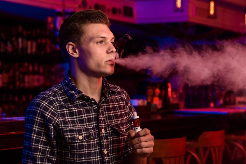 A person vaping, exhaling vapor, symbolizing the use of e-cigarettes. This image relates to e-cigarette and vaping injuries, highlighting the risks of defective devices and chemical exposure that can lead to serious health issues and potential legal claims.