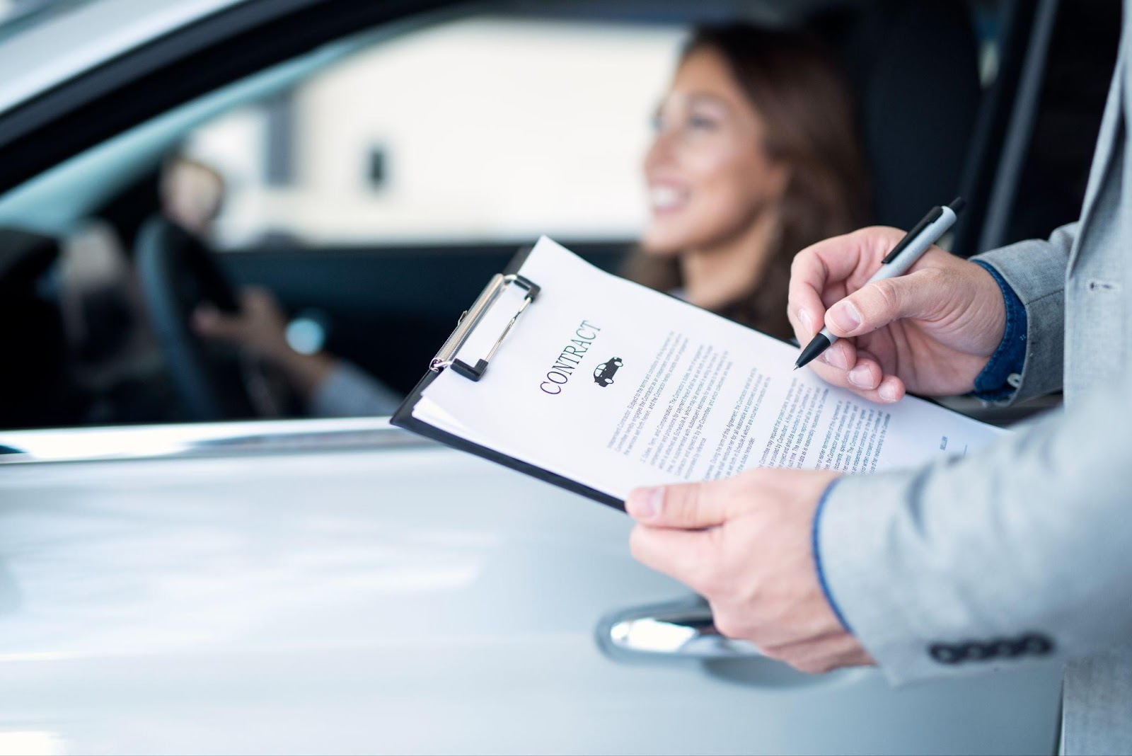 A woman sitting in her car while an insurance adjuster stands outside holding a contract, symbolizing the claims process. This image relates to dealing with insurance adjusters and navigating the insurance claims process, highlighting the importance of understanding policy terms and advocating for fair settlements.