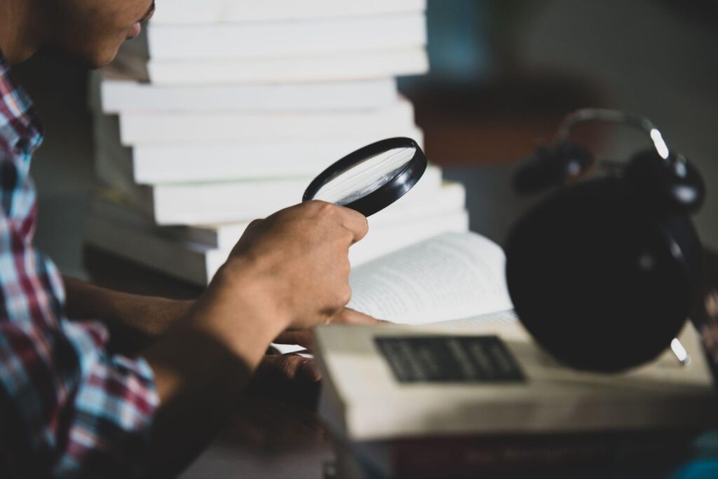 A person examining evidence through a magnifying glass, symbolizing careful analysis. This image relates to preparing for trial, highlighting the importance of gathering evidence and securing expert witness testimony to build a strong case.