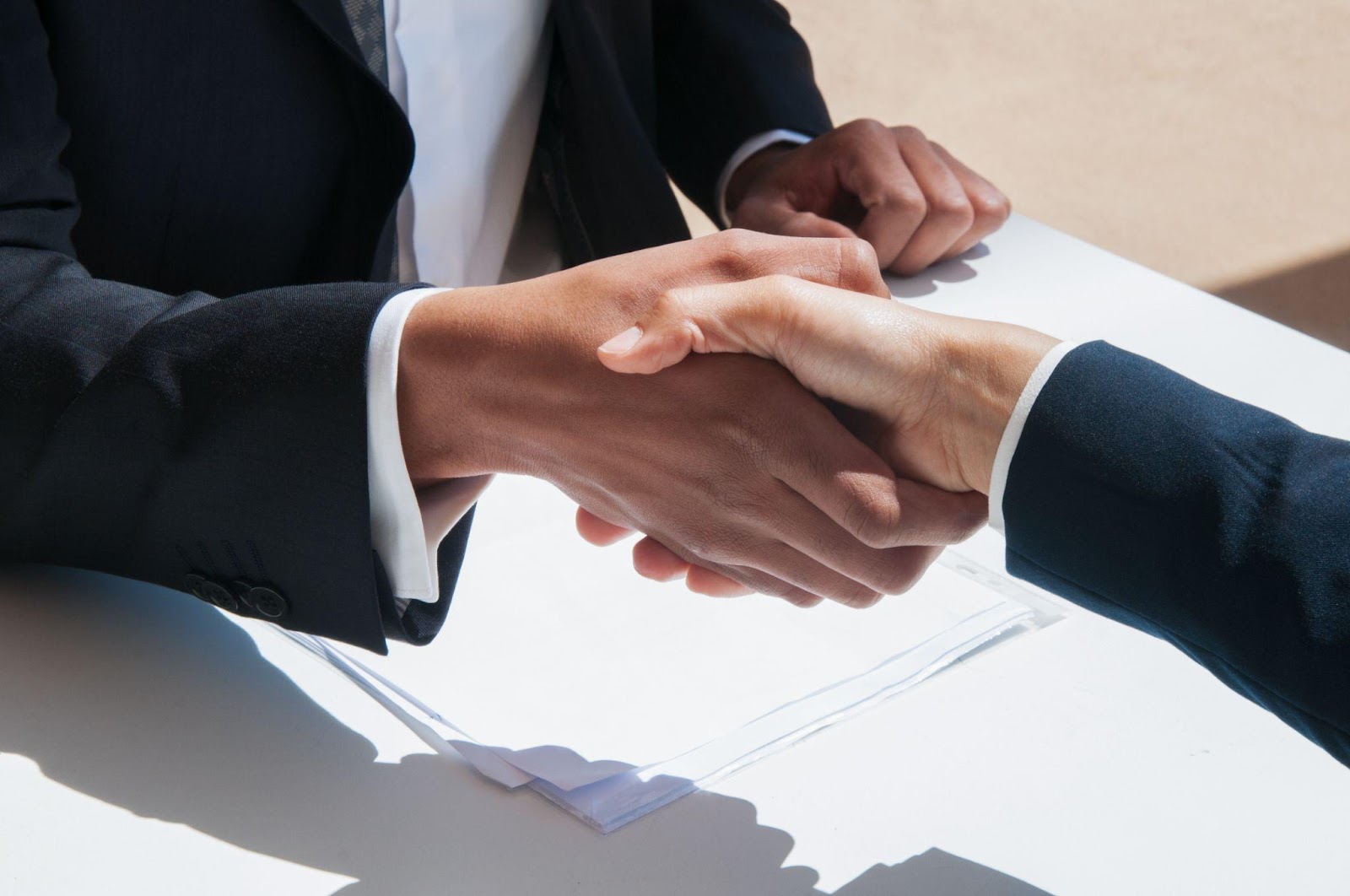 Close-up of two business professionals shaking hands over a table with documents, representing the critical role of legal representation in settlement negotiations.