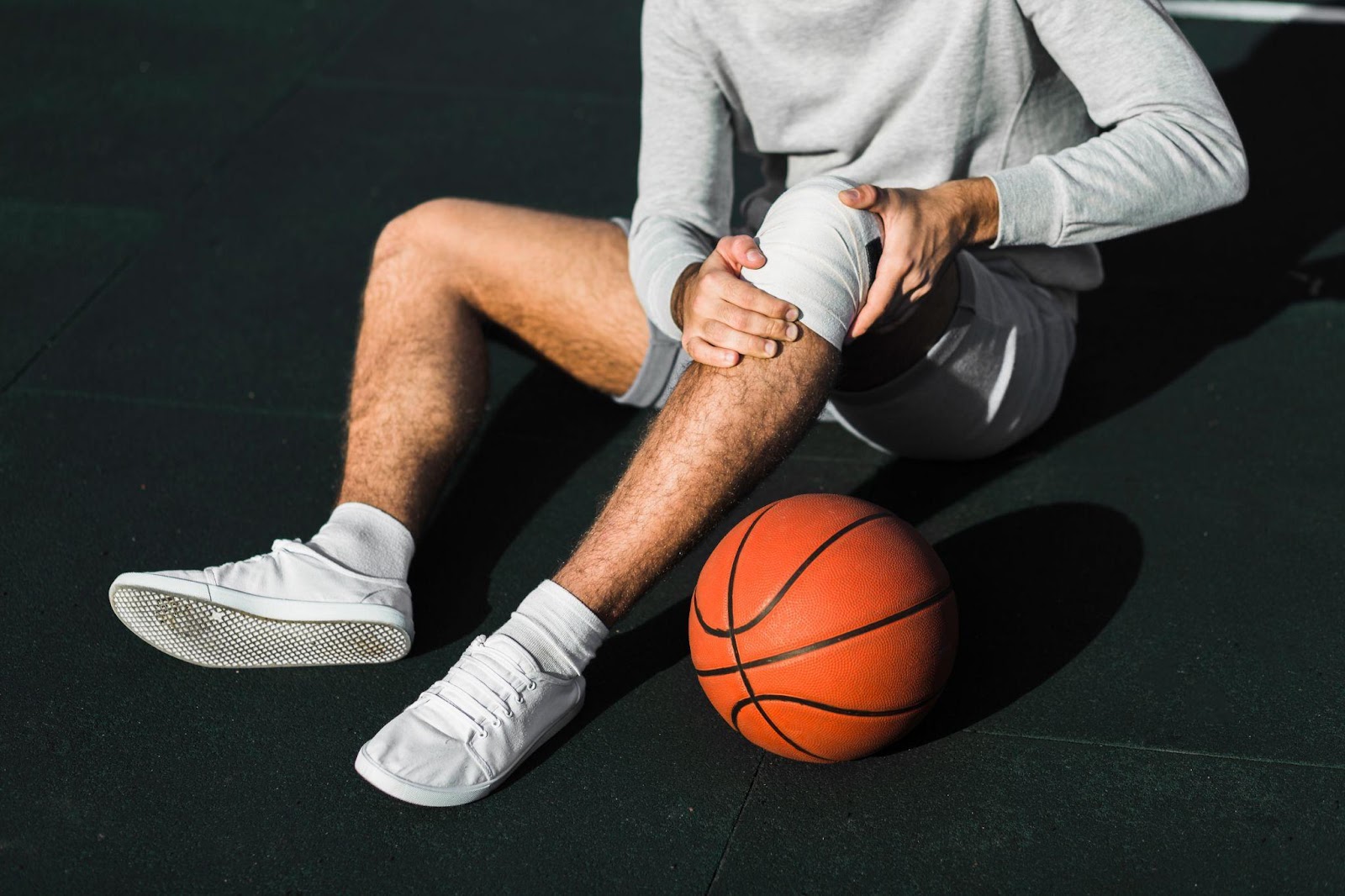 An athlete sitting on the court holding a knee injury, highlighting the discussion of sports injuries, including the liability of coaches, teams, and sports facilities in Alabama.