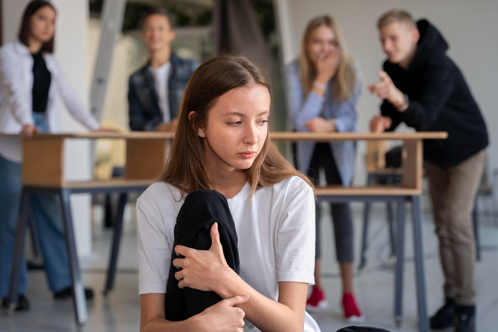 A person in the foreground appearing distressed and traumatized, while people in the background laugh, symbolizing a hostile work environment. This image relates to workplace violence, focusing on employer liability and workers' compensation for affected employees.