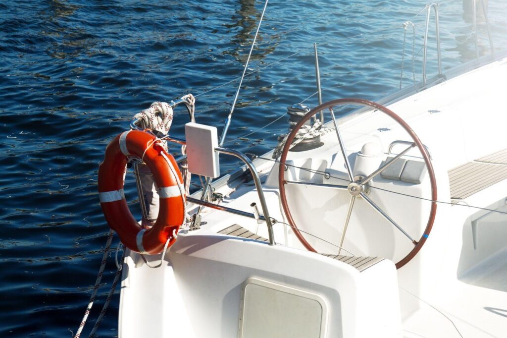 Close-up of a yacht's steering wheel and lifebuoy against a calm sea, highlighting boat and watercraft safety measures and tips for accident prevention.