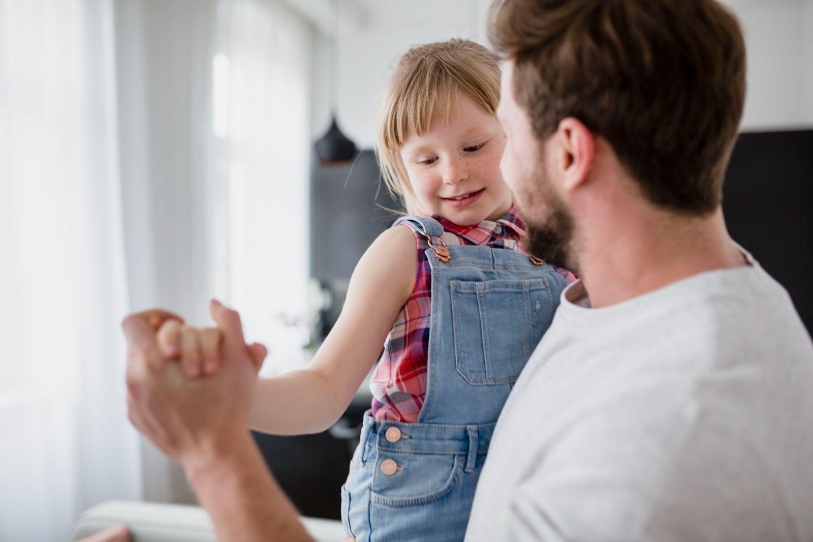 A father joyfully holding his daughter as she hangs playfully from his arms, representing the bond between father and child. The image highlights the topic of FAQs about fathers' rights in Alabama, emphasizing paternal involvement and legal rights.