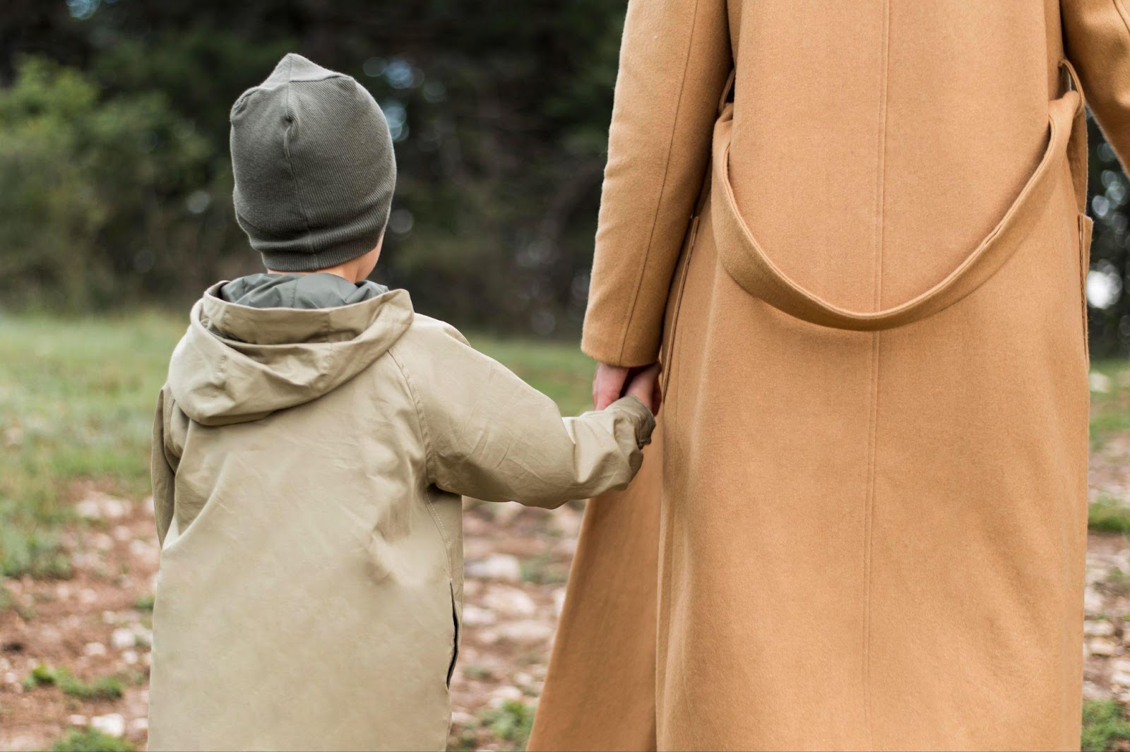 A rear view of a woman holding her child’s hand while walking outdoors, symbolizing the importance of preparing thoroughly for a child custody hearing in Alabama to safeguard the parent-child bond.