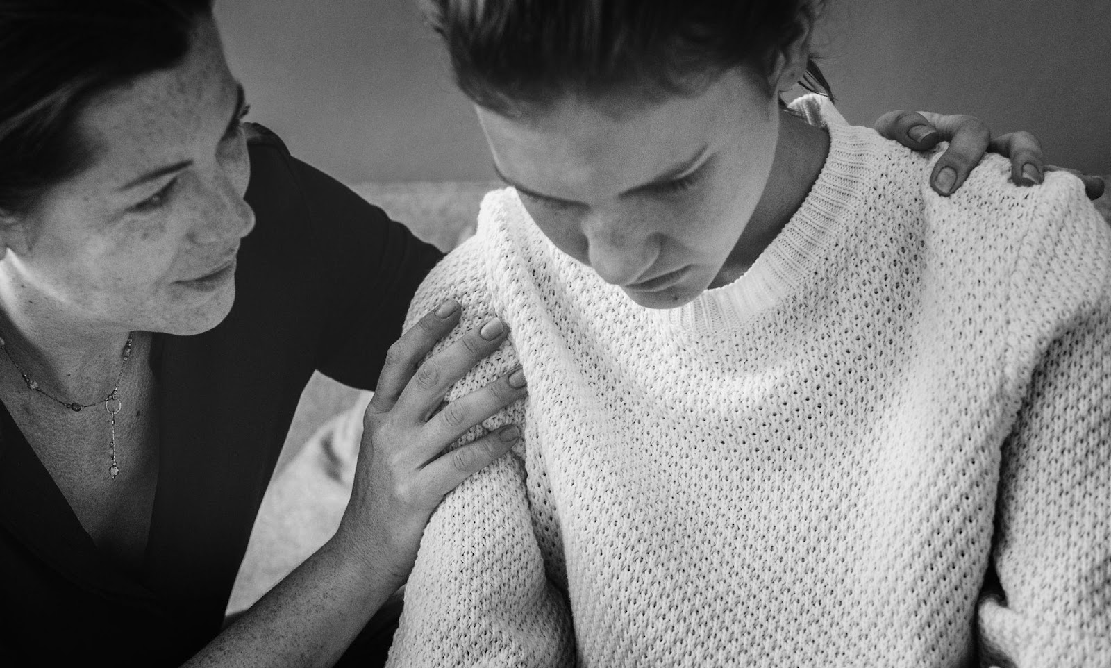 A black-and-white image showing a woman offering support to a younger person in distress. This visual represents the emotional challenges individuals face during difficult times, emphasizing the importance of empathy and understanding in family or interpersonal relationships.