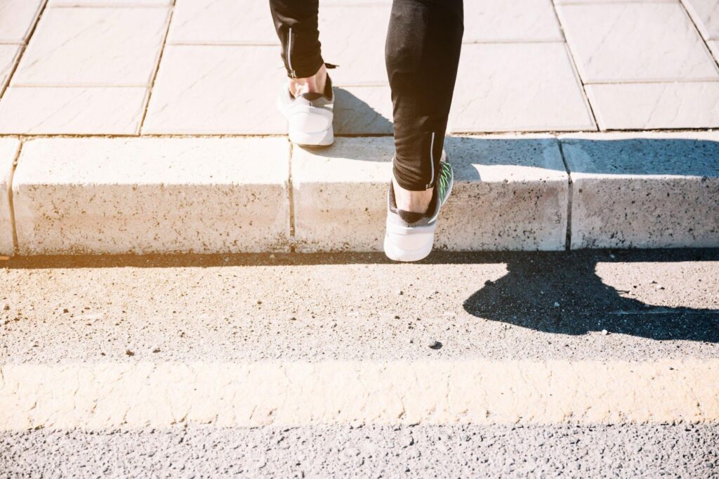 An image showing a person's legs stepping onto a sidewalk, representing the potential hazards of poorly maintained sidewalks. It highlights issues like slip and fall accidents, property upkeep, and legal liability related to pedestrian safety.