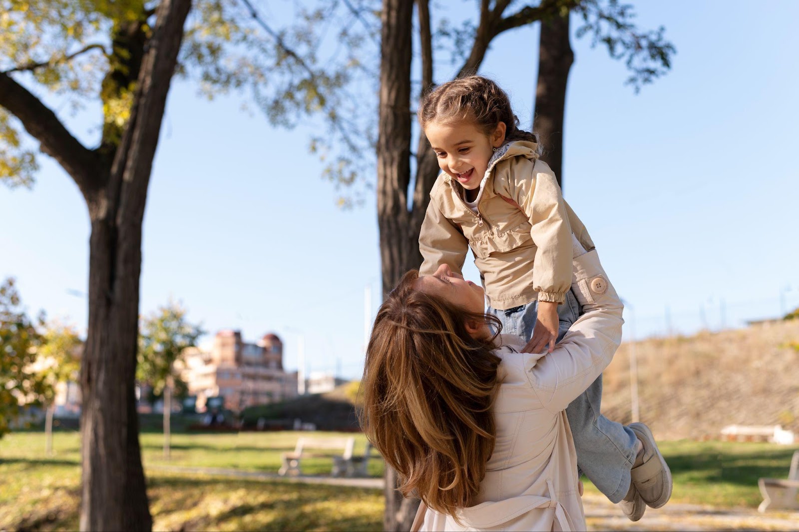 A joyful mother lifting her smiling child in a sunny park, symbolizing the importance of understanding Alabama child custody laws to prioritize a child’s well-being and happiness.