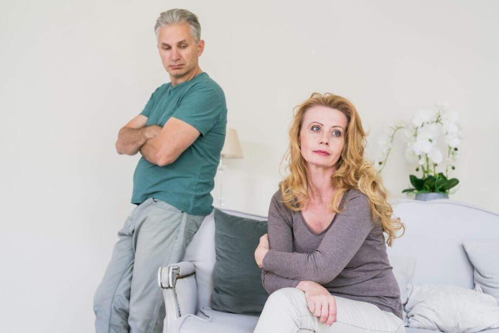 A middle-aged couple sits apart, their arms crossed and faces filled with tension, symbolizing marital strain. If you're considering ending a marriage, you may be wondering: how to get a divorce in Alabama? Understanding the legal process can help you navigate this challenging time.