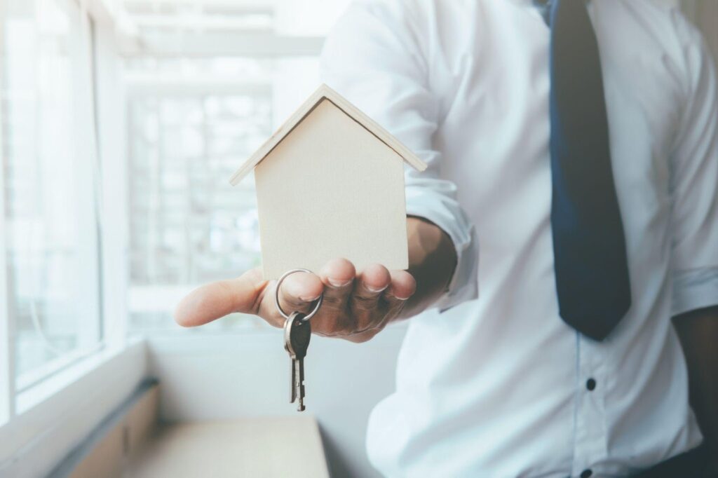 A lawyer handing over a small house model and keys, symbolizing the process of transferring property after death in Alabama.